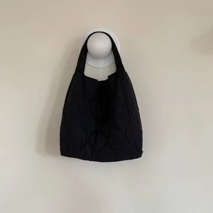 Detail of black quilted tote bag with soft padded texture hanging on a white wall hook