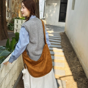 Gros plan du sac hobo en daim marron avec texture souple et pompon décoratif blanc