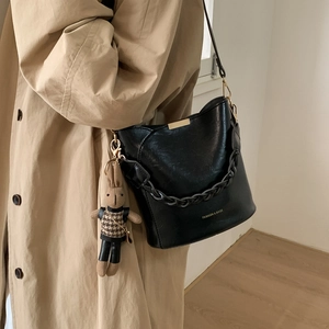 Detail of black leather bucket bag with woven handle and cute rabbit charm on tan coat