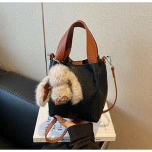 Detail of black pebbled leather bucket bag with brown handle and plush rabbit pendant