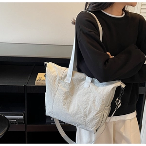 Detail of light gray tote bag with wrinkled texture, side drawstring, and adjustable strap