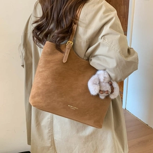 Detail of brown suede tote bag with leather strap and plush rabbit charm accessory