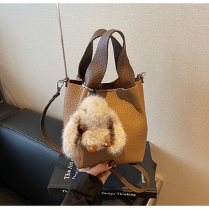 Close-up of brown pebble leather bucket bag with plush rabbit charm and crossbody strap