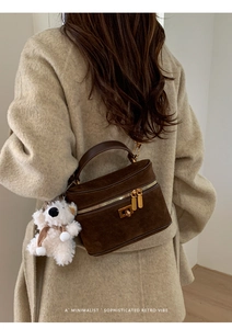 Détail du sac bandoulière en daim marron foncé avec ferrures dorées et breloque ours blanc