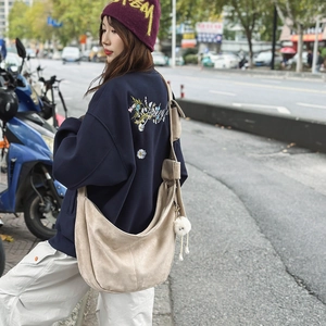 Détail d'un grand sac bandoulière en daim beige avec sangle large et pompon en peluche