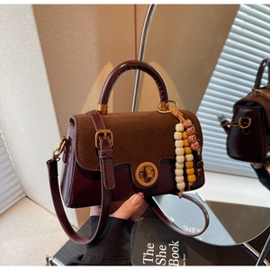 Detail of burgundy textured leather handbag with gold clasp and bohemian bead charm