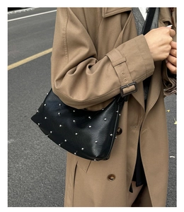 Detail of a chic black shoulder bag with silver rivets worn over a camel trench coat