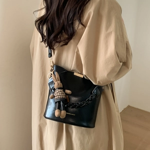 Detail of black leather bucket bag featuring a cute rabbit charm and woven chain strap