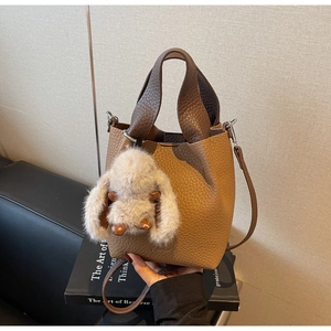 Detail of a brown lychee leather bucket bag with a cute plush rabbit charm on a book