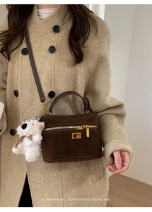Sac boîte marron foncé avec détails dorés et breloque peluche sur manteau tweed