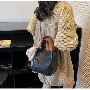 Detail of mini bucket bag in black pebble leather with caramel handles and plush charm