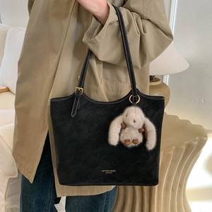 Detail of black leather tote bag with brand logo and cute white plush bunny charm