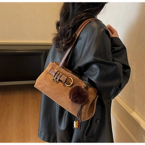 Macro shot of brown suede shoulder bag featuring retro metal buckle and plush ball charm