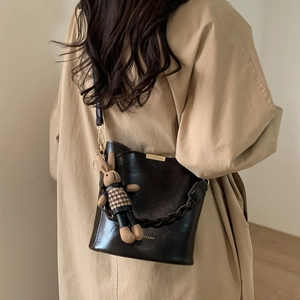 Detail of dark brown bucket bag with rabbit charm and woven handle on beige trench coat