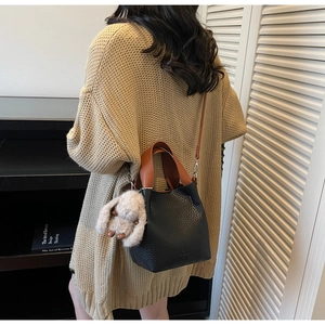 Detail of black pebbled leather bucket bag with brown handle and plush rabbit charm
