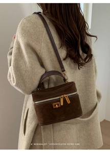 Détail du sac boîte en daim marron foncé avec fermeture éclair dorée et poignée en cuir