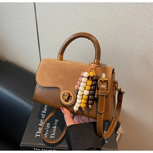 Detail of a brown textured tote bag featuring a metal lock and colorful beaded charm