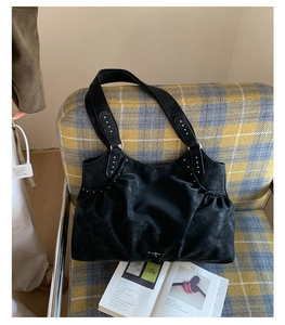 Detail of black suede tote bag featuring silver rivet accents and slouchy design