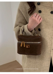 Détail du vanity-case marron foncé montrant les zips dorés et la texture mate premium