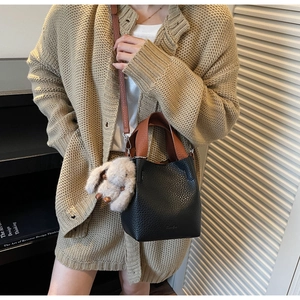 Close-up of black leather bucket bag with brown straps and white plush bunny charm