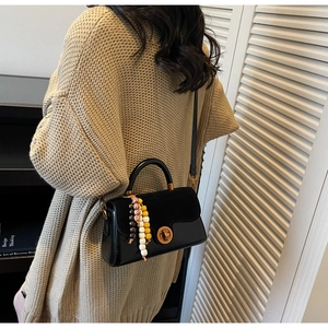 Detail of black crossbody bag with gold lock and colorful beads on a beige sweater