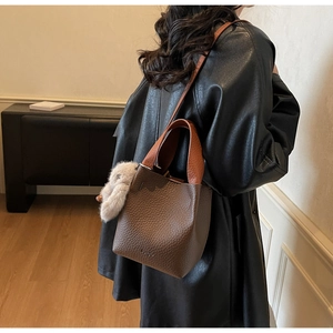 Close-up of deep brown pebble leather bucket bag with orange handle and plush rabbit charm