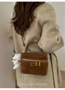 Sac boîte en daim marron avec charm peluche blanche porté sur un manteau