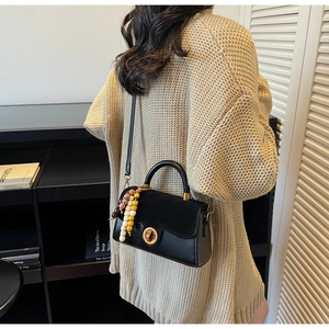 Detail of black crossbody bag with gold ring lock and colorful beaded charm accessory