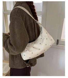 Detail view of cream crescent bag with silver rivets and wide strap shown on shoulder