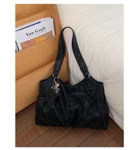 Close-up of black suede tote bag featuring silver rivet details and star charm accessory