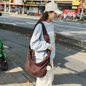Détail du sac hobo en daim brossé marron foncé avec un charme en peluche à l'extérieur