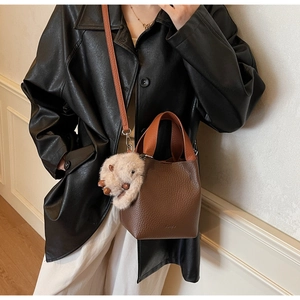 Detail of dark brown leather bucket bag with orange handle and cute plush charm