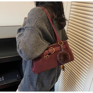 Detail of burgundy suede shoulder bag with gold buckle and plush pom-pom charm decoration