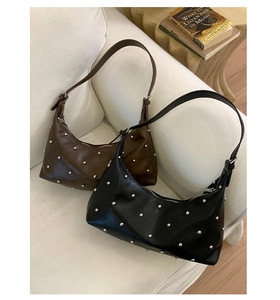 Close-up of black and coffee rivet shoulder bags on a white sofa in a lifestyle setting