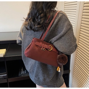 Detail of burgundy shoulder bag with belt buckle, plush ball and wooden bead charms