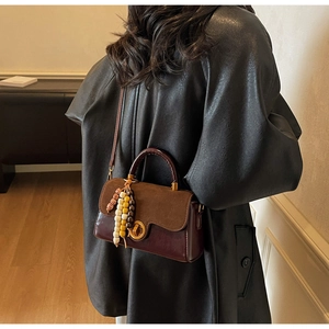 Detail view of retro square handbag with brown flap, wine red body and wood bead tassel
