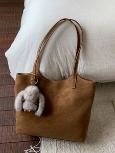 Brown suede tote bag with a cute plush rabbit charm on a warm lifestyle background