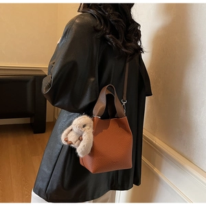 Side view of a brown leather bucket bag with a plush bunny charm worn on shoulder
