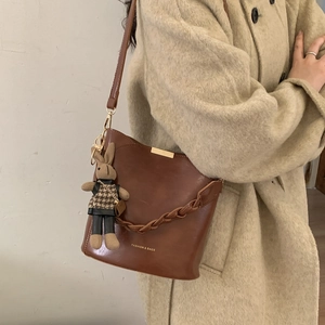 Brown vintage leather bucket bag featuring unique woven strap and cute rabbit pendant