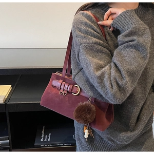 Detail of burgundy suede shoulder bag featuring metal buckle and plush pompom charm