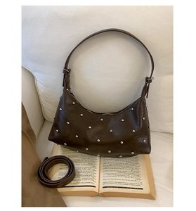 Detail of dark brown rivet dumpling bag with adjustable strap and vintage texture