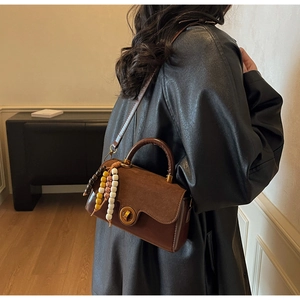 Detail view of brown leather and suede crossbody bag with retro metal clasp and beads