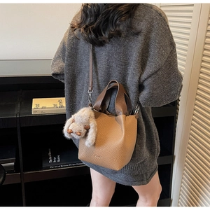 Close-up of brown lychee grain bucket bag with a plush rabbit charm on side