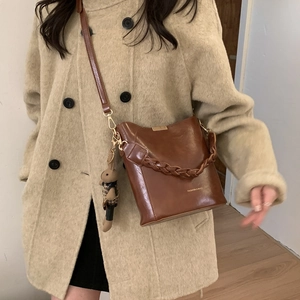 Detail of retro brown bucket bag with braided handle and cute teddy bear charm