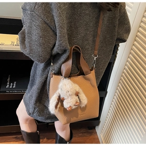 Brown lychee leather bucket bag with cute rabbit charm worn over a grey knit sweater