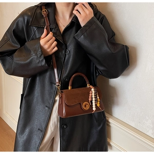 Detail of dark brown retro leather handbag with suede flap and bohemian bead charm