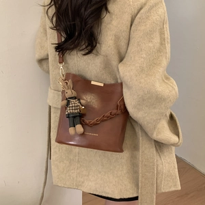 Brown leather crossbody bag with woven handle and rabbit charm on model beige coat
