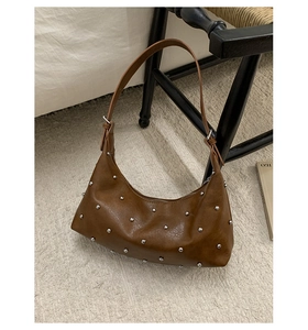 Detail view of brown crescent shoulder bag with silver rivet studs on textured leather