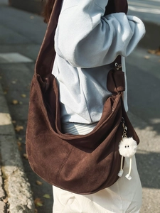 Sac hobo marron en suédine avec breloque monstre présenté dans un décor extérieur naturel