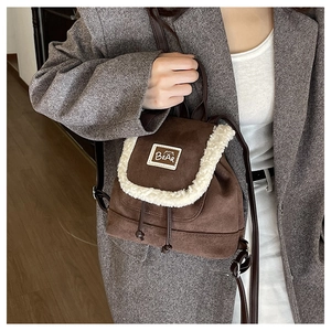 Detail of mini brown suede backpack with faux fur trim and bear logo on a grey blazer